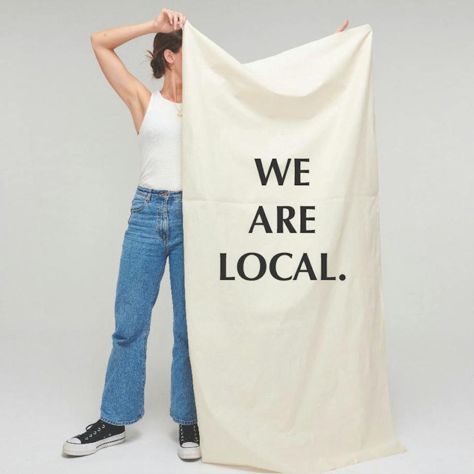 Person holds large canvas with 'We Are Local' printed on front.