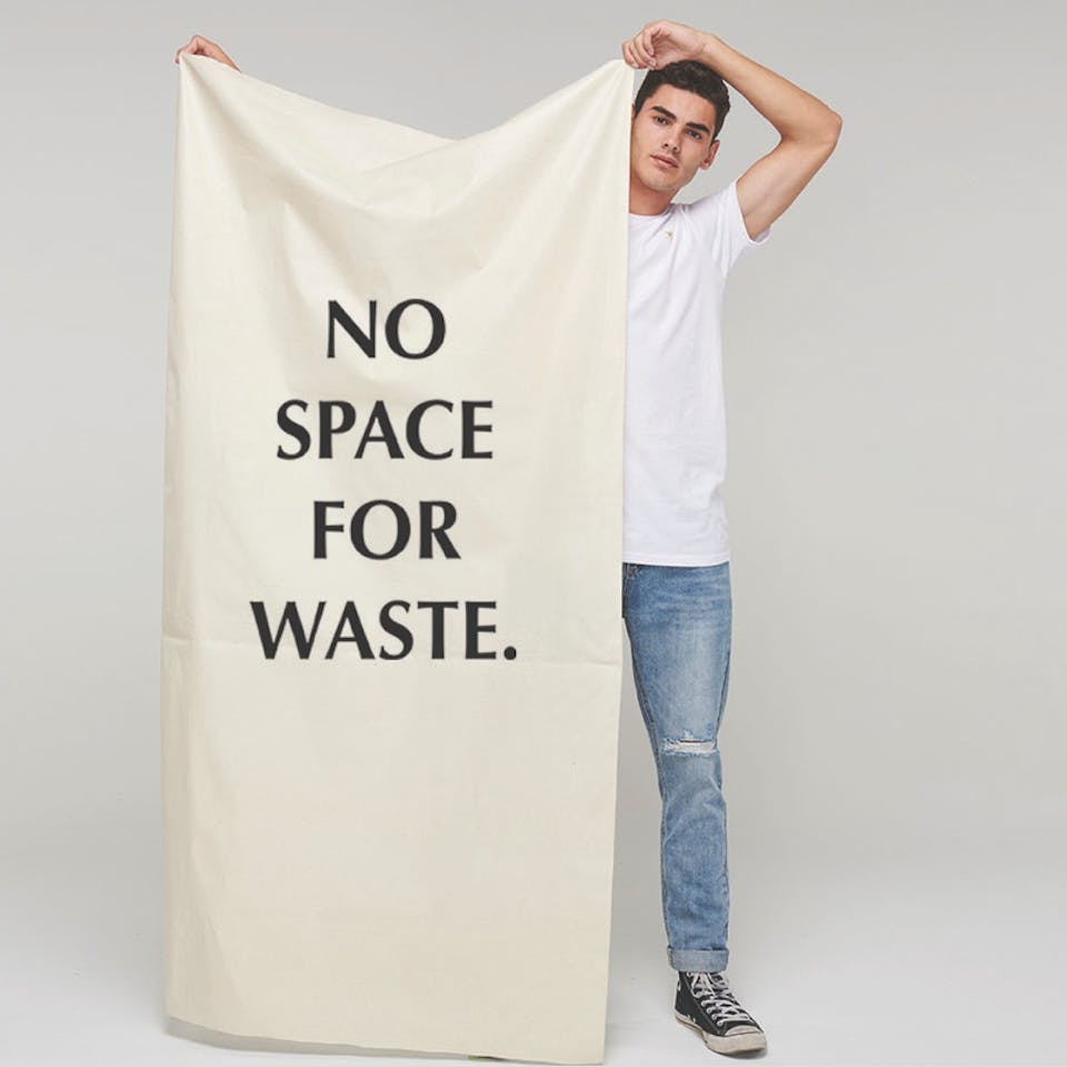 Person holds large canvas with 'No space for waste.' on front.